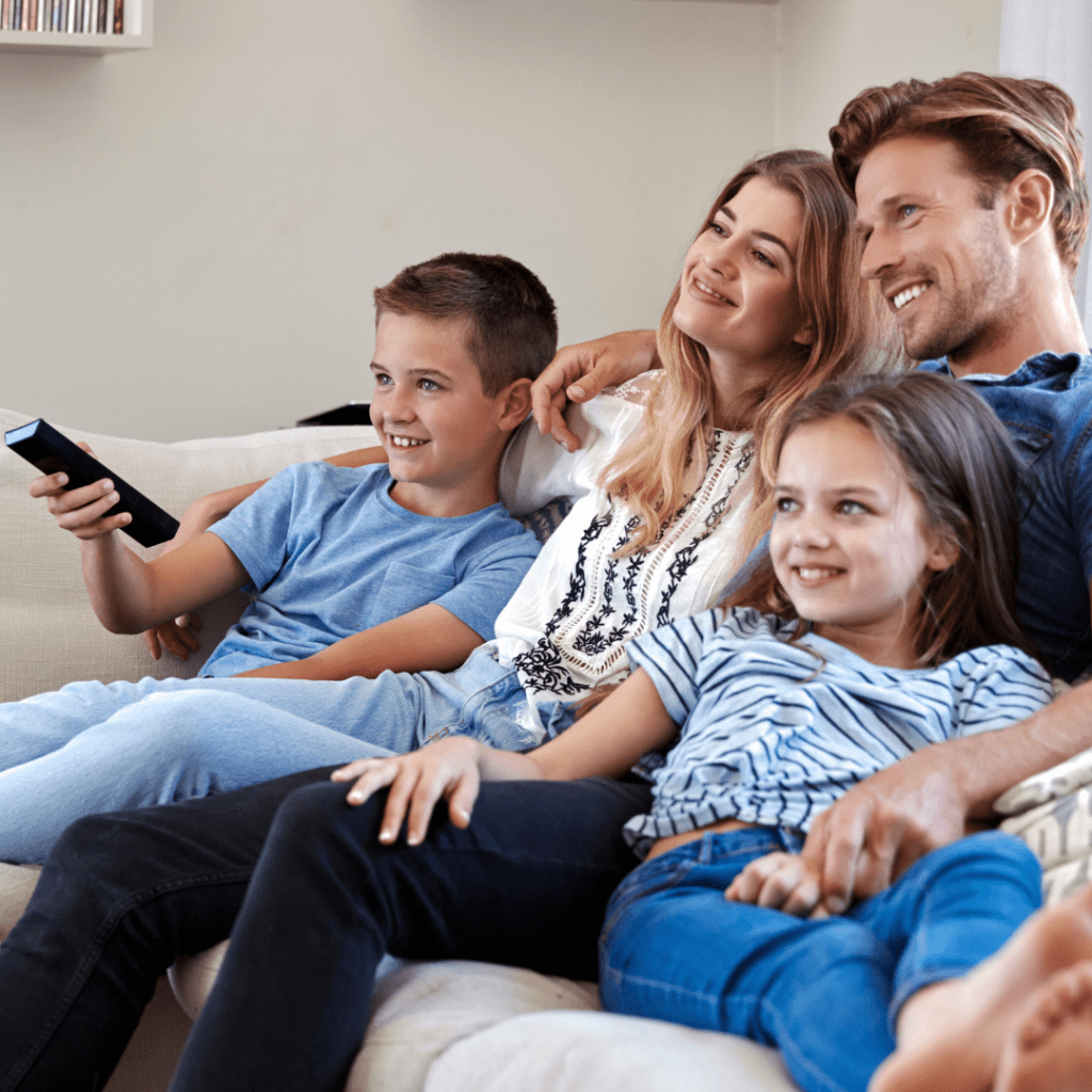 A young family all close and relaxed on a couch enjoying a movie
