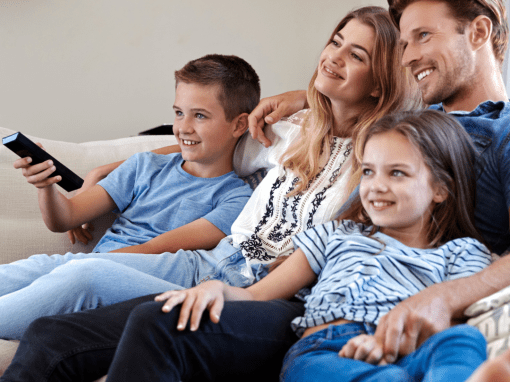 A young family all close and relaxed on a couch enjoying a movie