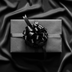 Black wrapped gift box with black ribbon on black silk background for Black Friday Amazon device deals article.