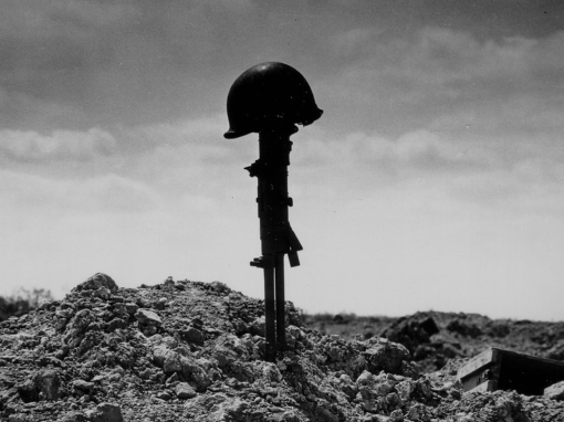 Black and white image showing a rifle placed barrel-down in the ground with a helmet resting on its butt, symbolizing a fallen soldier’s sacrifice.