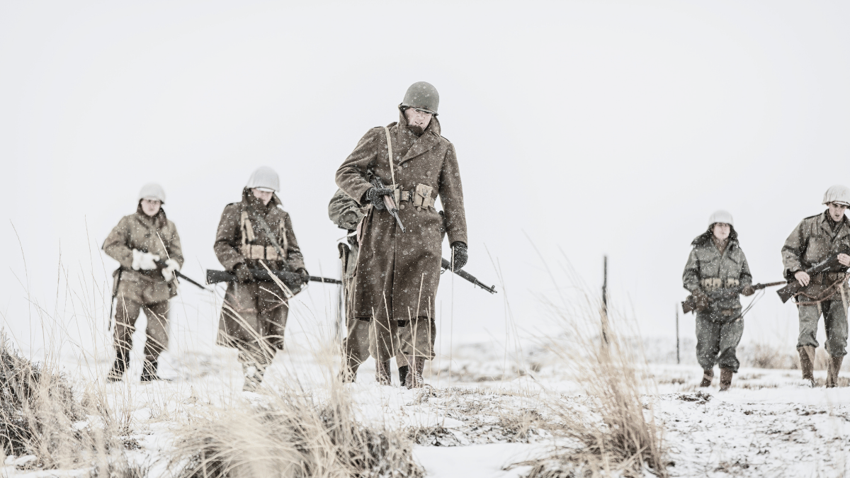 A small column of World War II soldiers marches up a snowy road on a harsh winter day, symbolizing the extreme conditions and sacrifices of frontline troops.