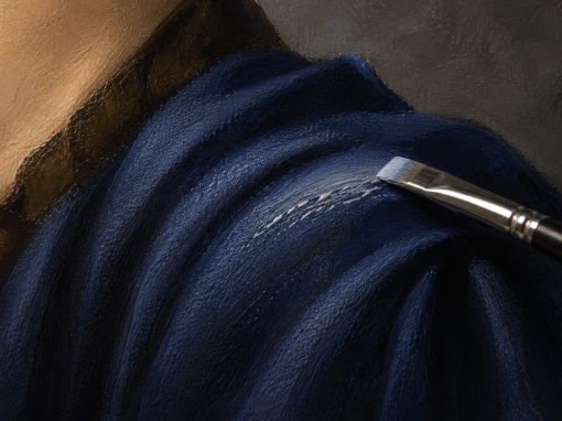 Close-up of thin oil paint separating into streaks and elongated beads while a flat brush applies a light blue highlight across dark blue fabric folds in an oil painting.